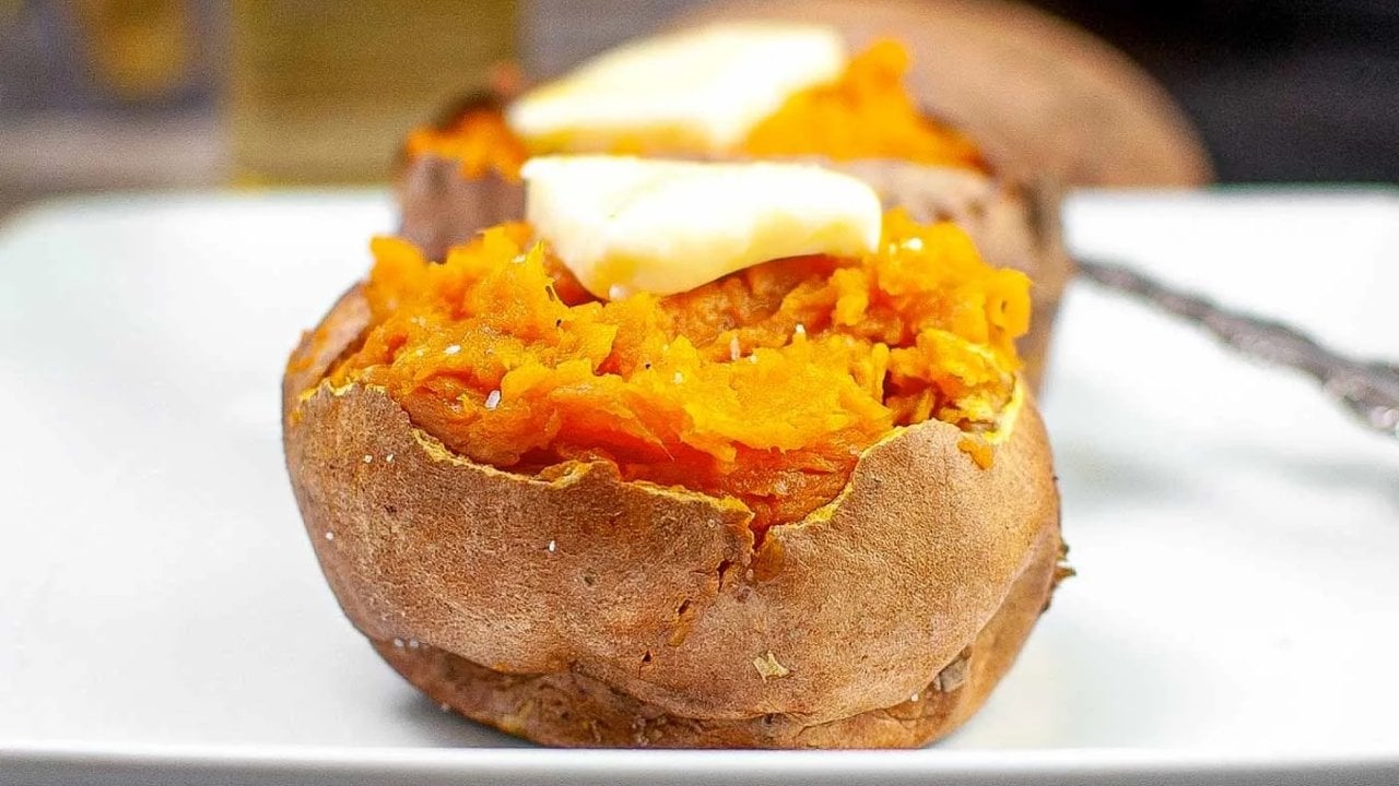 A baked sweet potato split open on a plate, topped with melting butter.