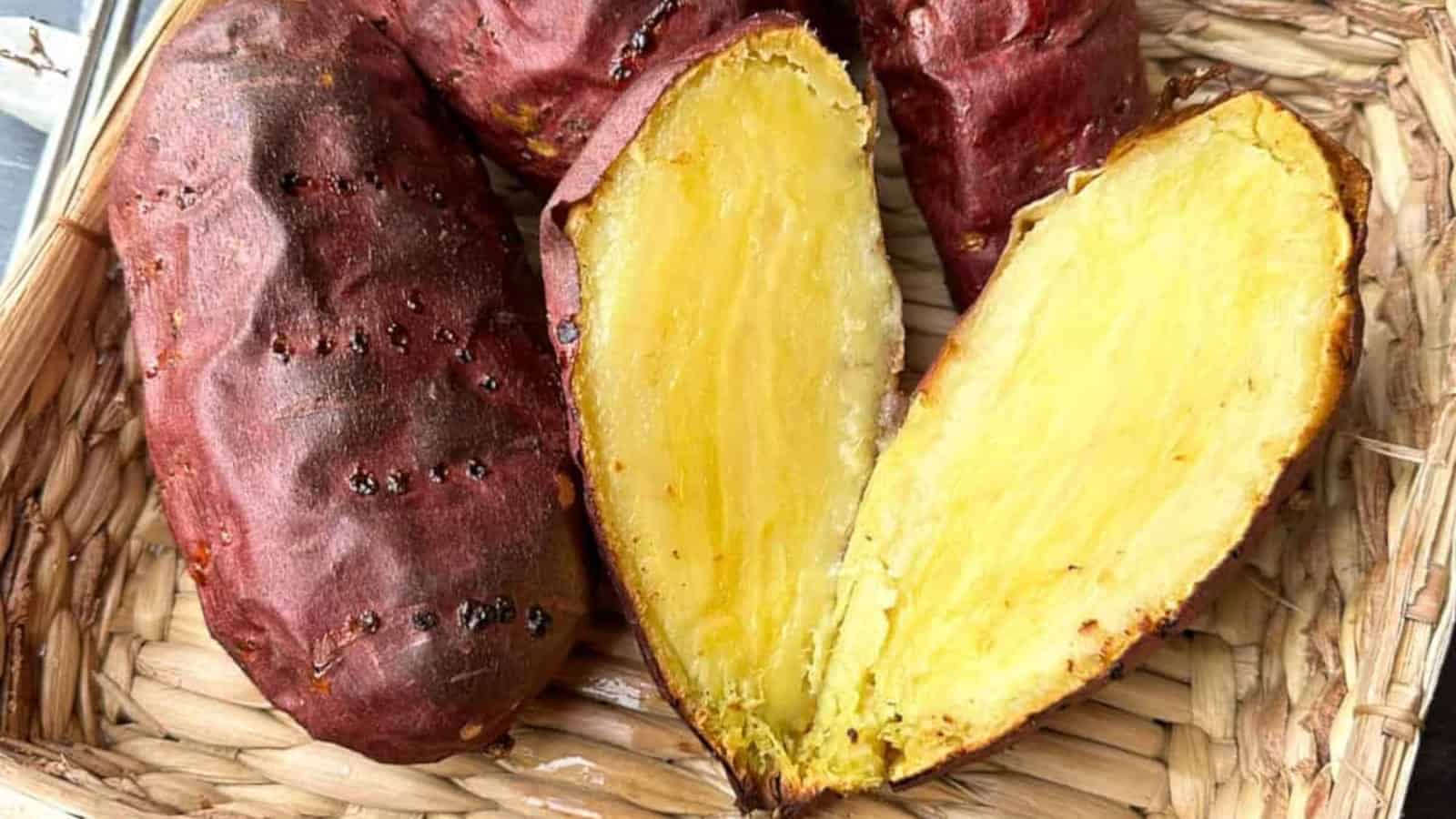 A roasted sweet potato with reddish-purple skin, cut in half to show its yellow, soft interior, placed in a woven basket.