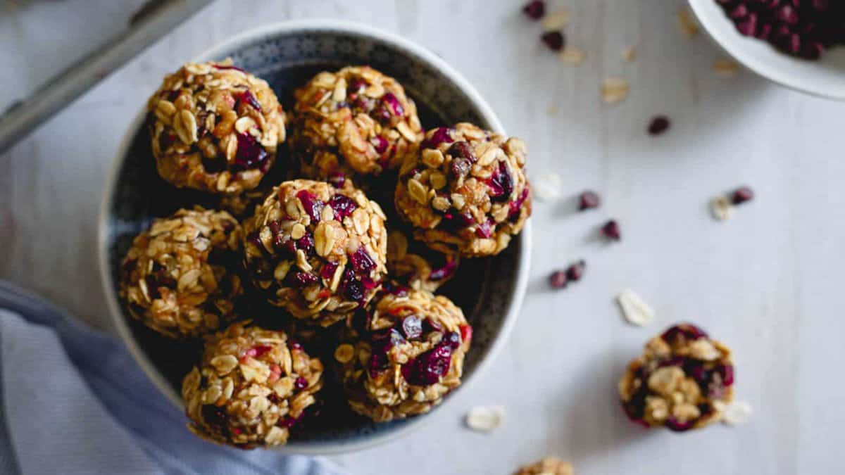 A bowl filled with oat and berry energy bites sits on a light surface, with a few scattered bites and oats around it.