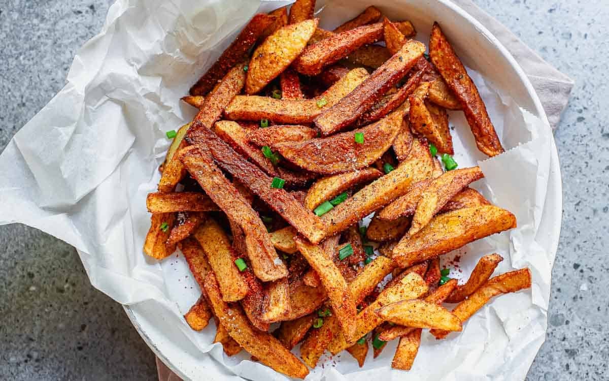 A bowl lined with parchment paper filled with seasoned potato fries, garnished with chopped green onions.
