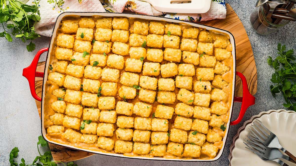 A rectangular casserole dish filled with tater tot hotdish, topped with evenly arranged golden tater tots and sprinkled with herbs.