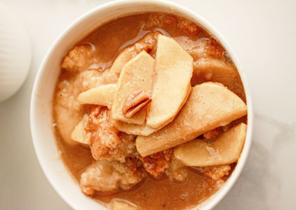 A bowl of apple slices and pecan pieces in a cinnamon-brown sauce, resembling a baked dessert or cobbler.