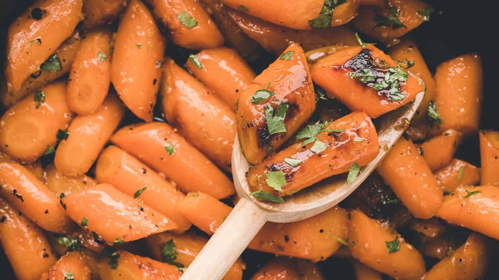 Glazed carrot slices garnished with chopped parsley, with a wooden spoon lifting a few pieces from the dish.