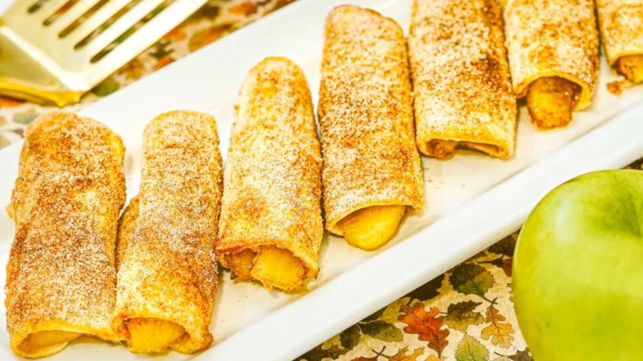 A row of cinnamon sugar-coated rolled pastries filled with apple, arranged on a rectangular white plate.