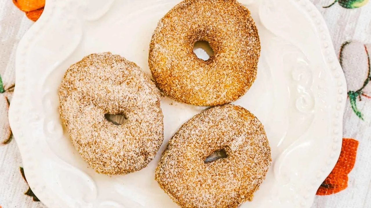 Three sugar-coated doughnuts are arranged on a white decorative plate.
