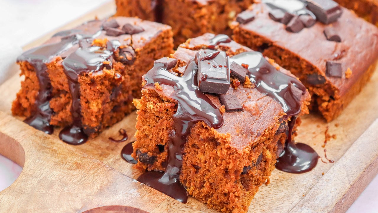 Chocolate cake slices topped with pieces of chocolate and drizzled with chocolate sauce on a wooden board.
