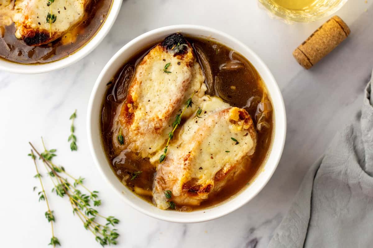 A bowl of French onion soup topped with toasted bread and melted cheese, garnished with fresh thyme, placed on a marble surface.