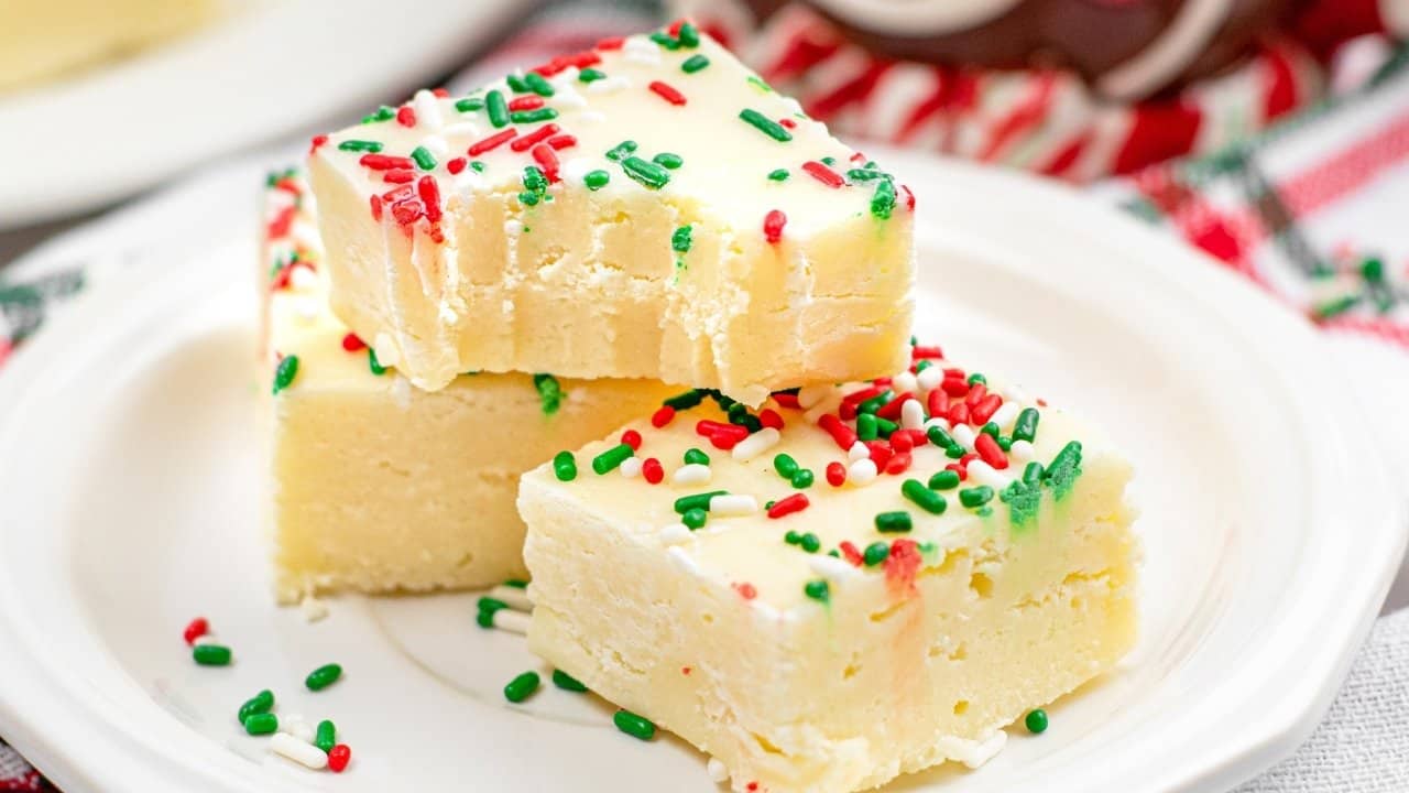 Three pieces of white fudge topped with red, green, and white sprinkles are stacked on a white plate.