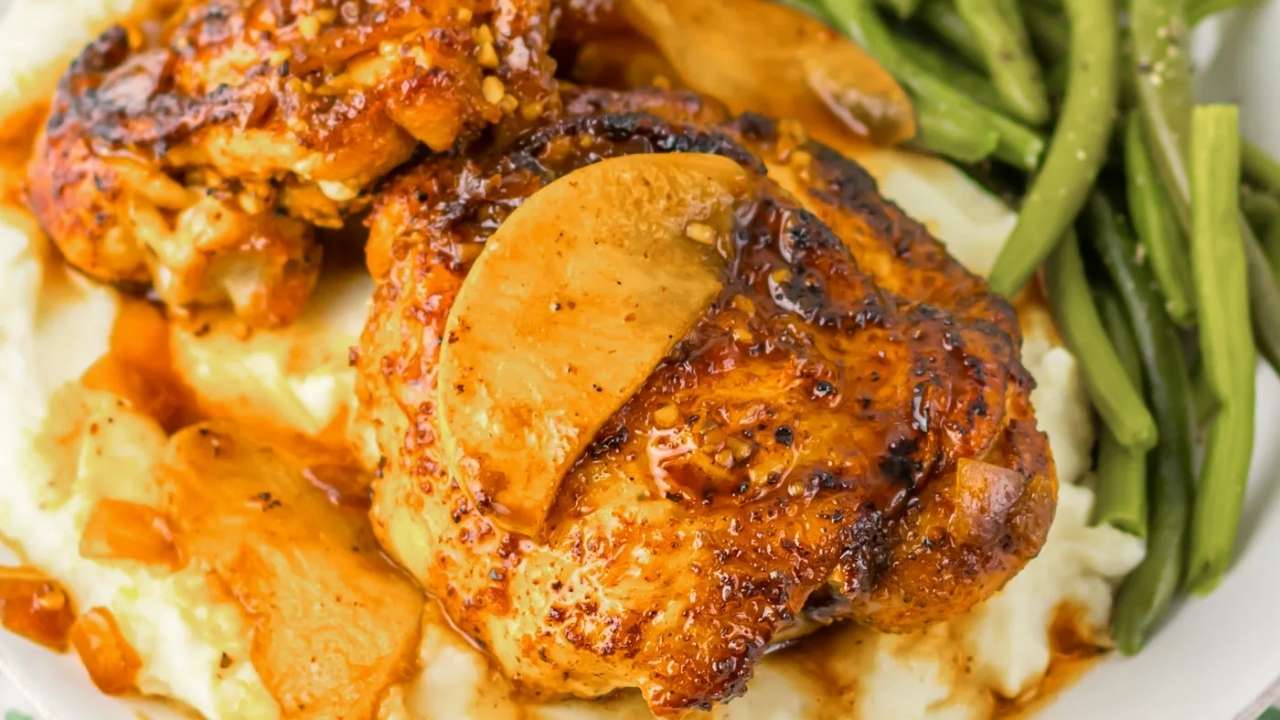 Grilled chicken thighs with apple slices on mashed potatoes, served alongside cooked green beans.