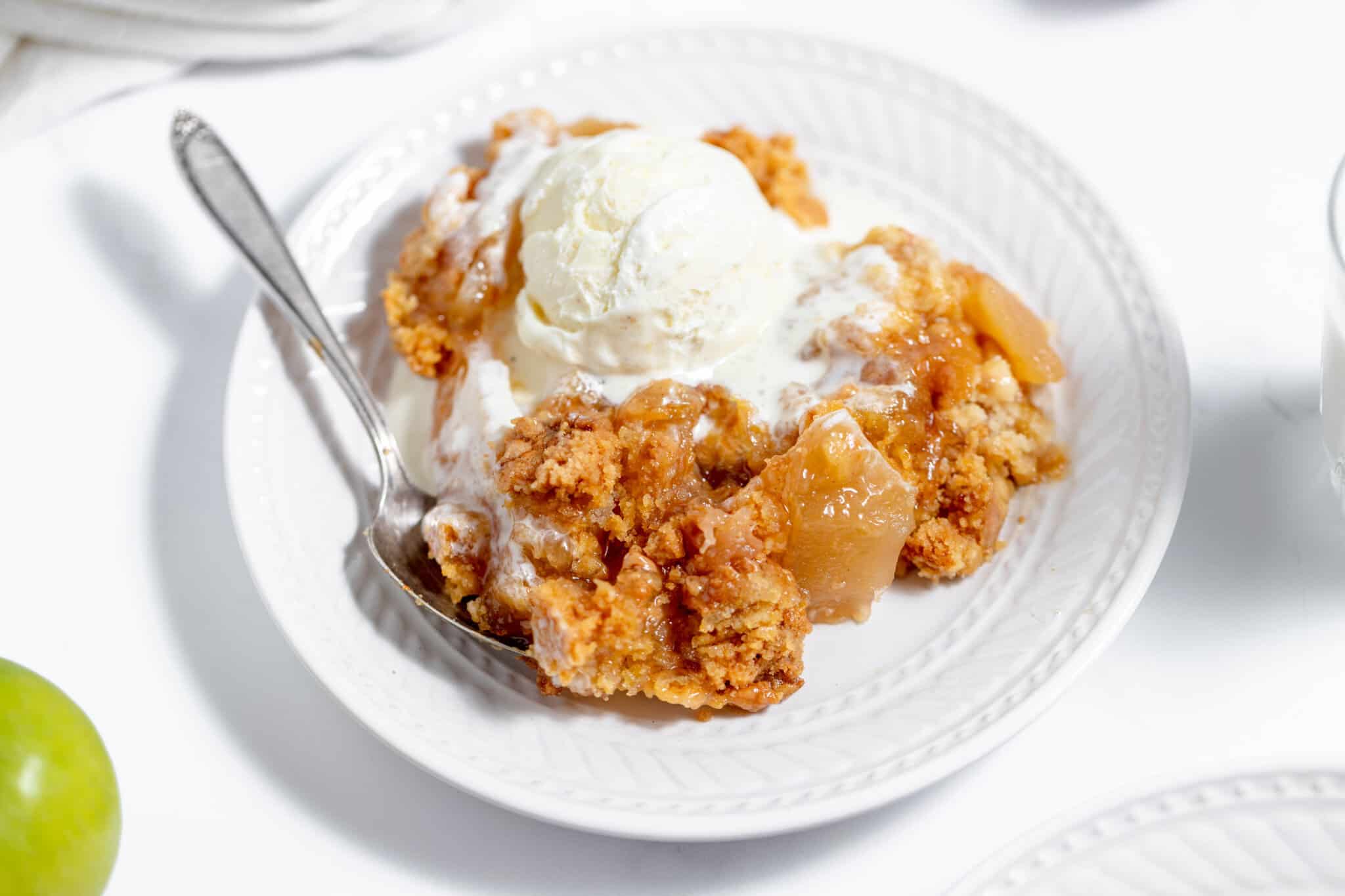 A plate of apple cobbler topped with a scoop of vanilla ice cream, with a spoon resting on the plate.