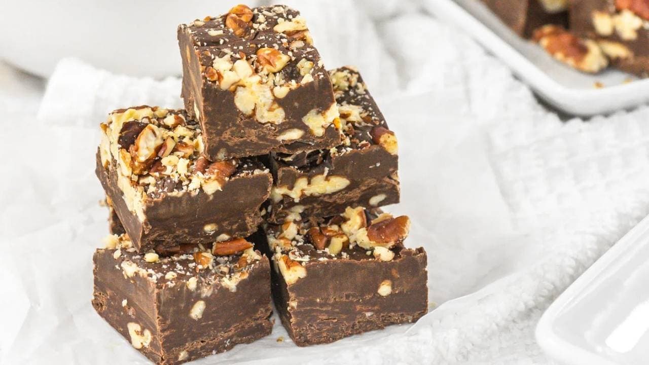 A stack of chocolate fudge pieces with chopped nuts on top, placed on white parchment paper.