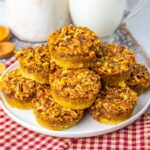 A plate of mini pecan pies stacked on top of each other, sitting on a red checkered cloth, with milk and a jar in the background.