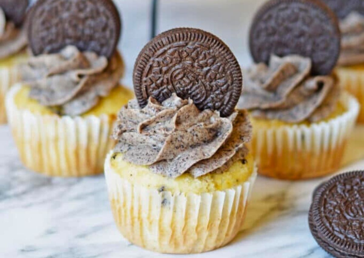 Vanilla cupcakes topped with cookies and cream frosting and decorated with a chocolate sandwich cookie on top, arranged on a marble surface.