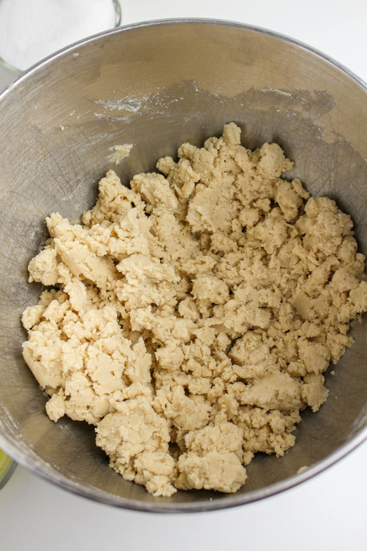 A metal mixing bowl filled with raw cookie dough on a white surface.