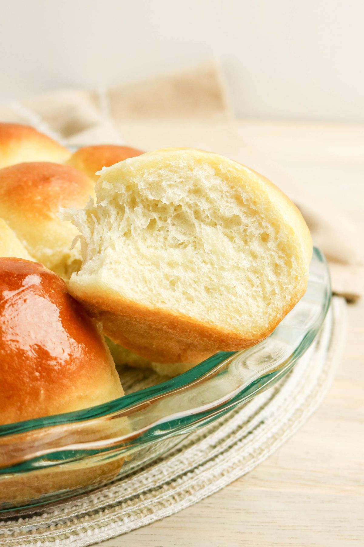 A close-up of a glass dish with several golden brown dinner rolls, one of which is partially torn open to show its soft, fluffy interior.