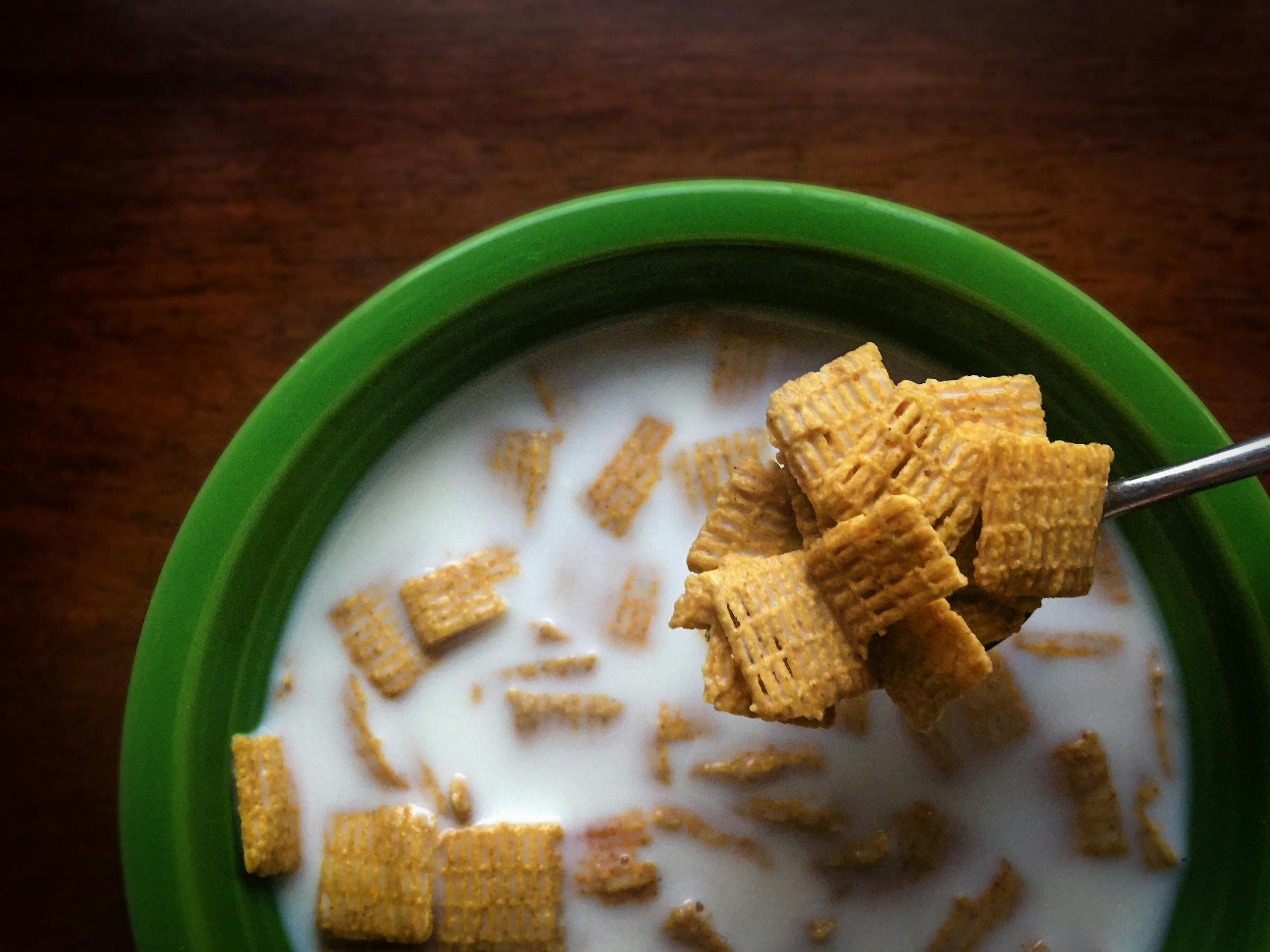 Top view of Chex cereal in milk inside a green bowl, showcasing a spoonful of cereal.