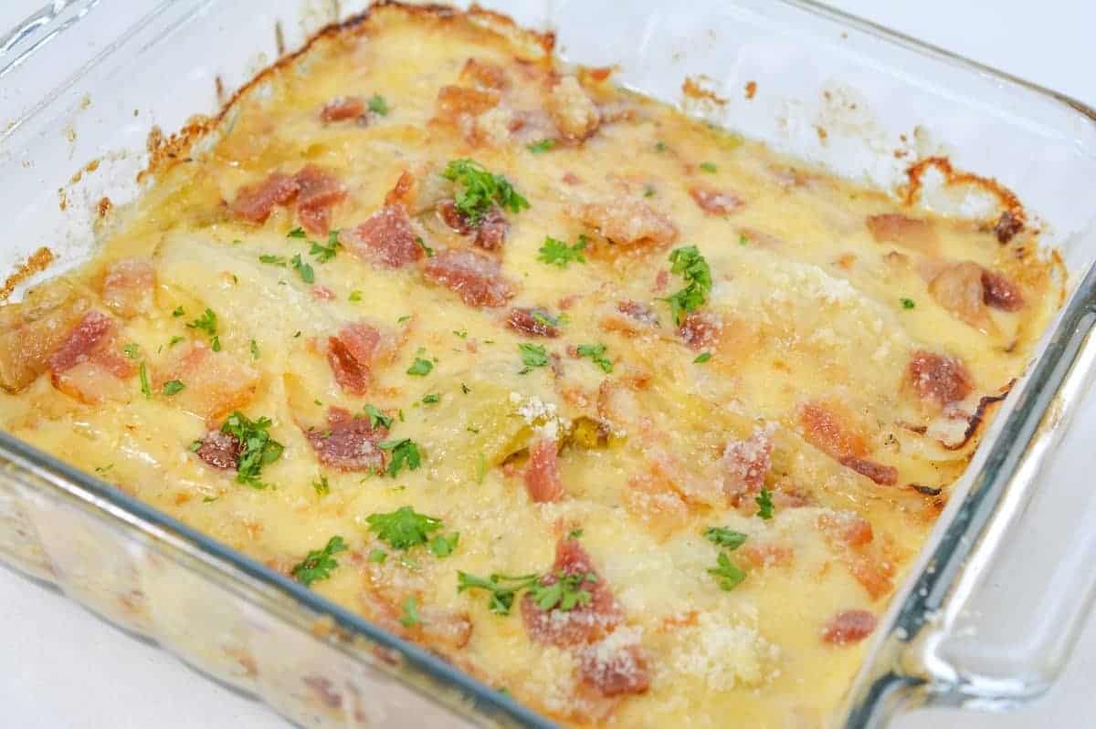 A glass baking dish filled with baked cheesy casserole topped with chopped bacon and parsley.