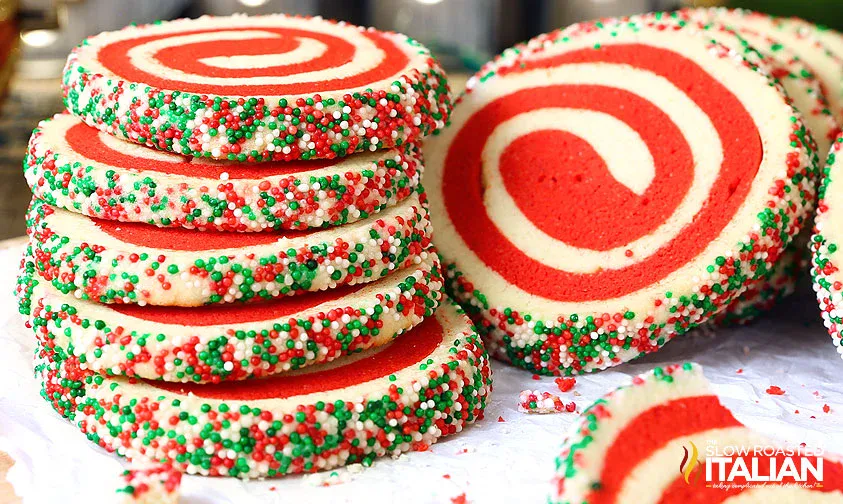 Stack of red and white pinwheel cookies with edges coated in red, white, and green sprinkles, displayed on a white surface.