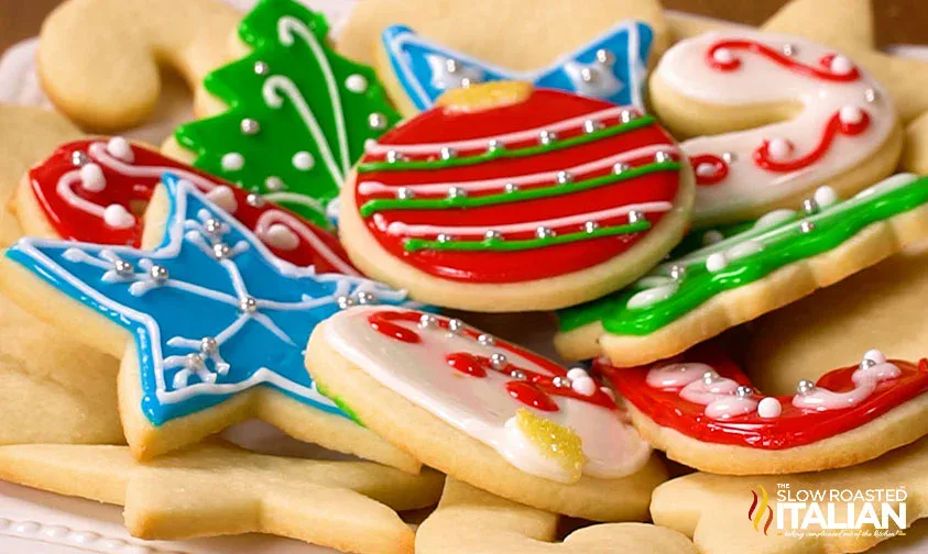 A plate of decorated Christmas sugar cookies in various shapes, including stars, trees, and ornaments, with colorful icing and sprinkles.