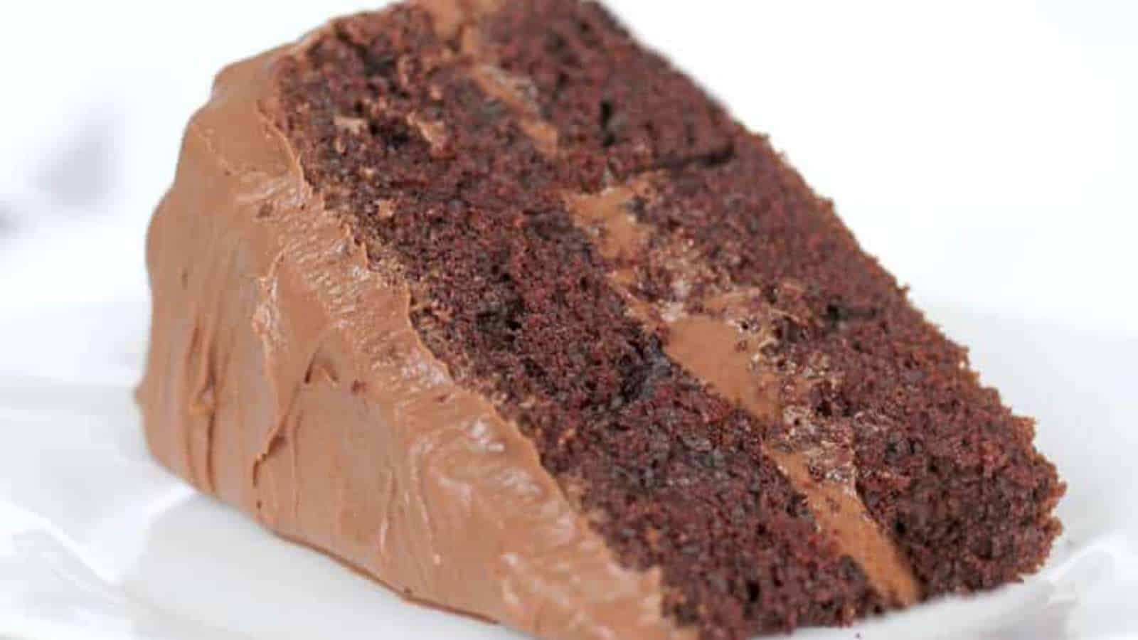 A close-up of a slice of chocolate layer cake with chocolate frosting on a white plate.