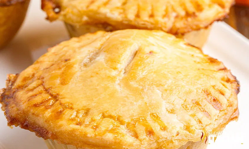 Close-up of two golden-brown baked pies with crimped edges and flaky crusts on a white surface.