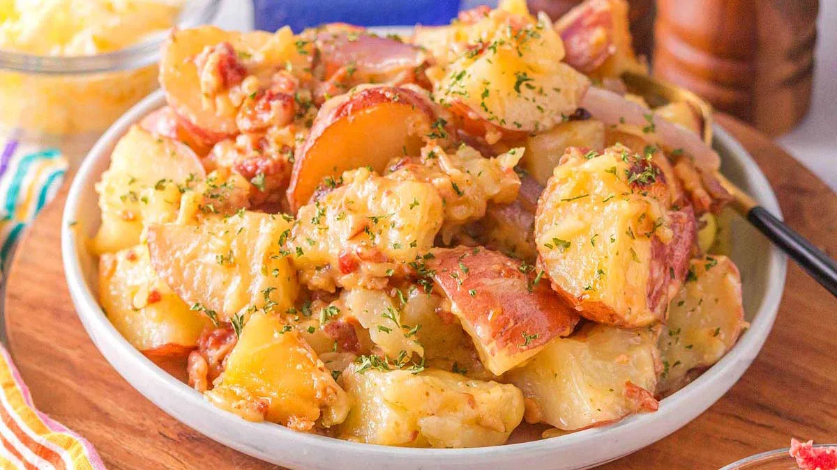 A bowl of cheesy ranch potatoes with chopped bacon and herbs, served on a wooden surface.