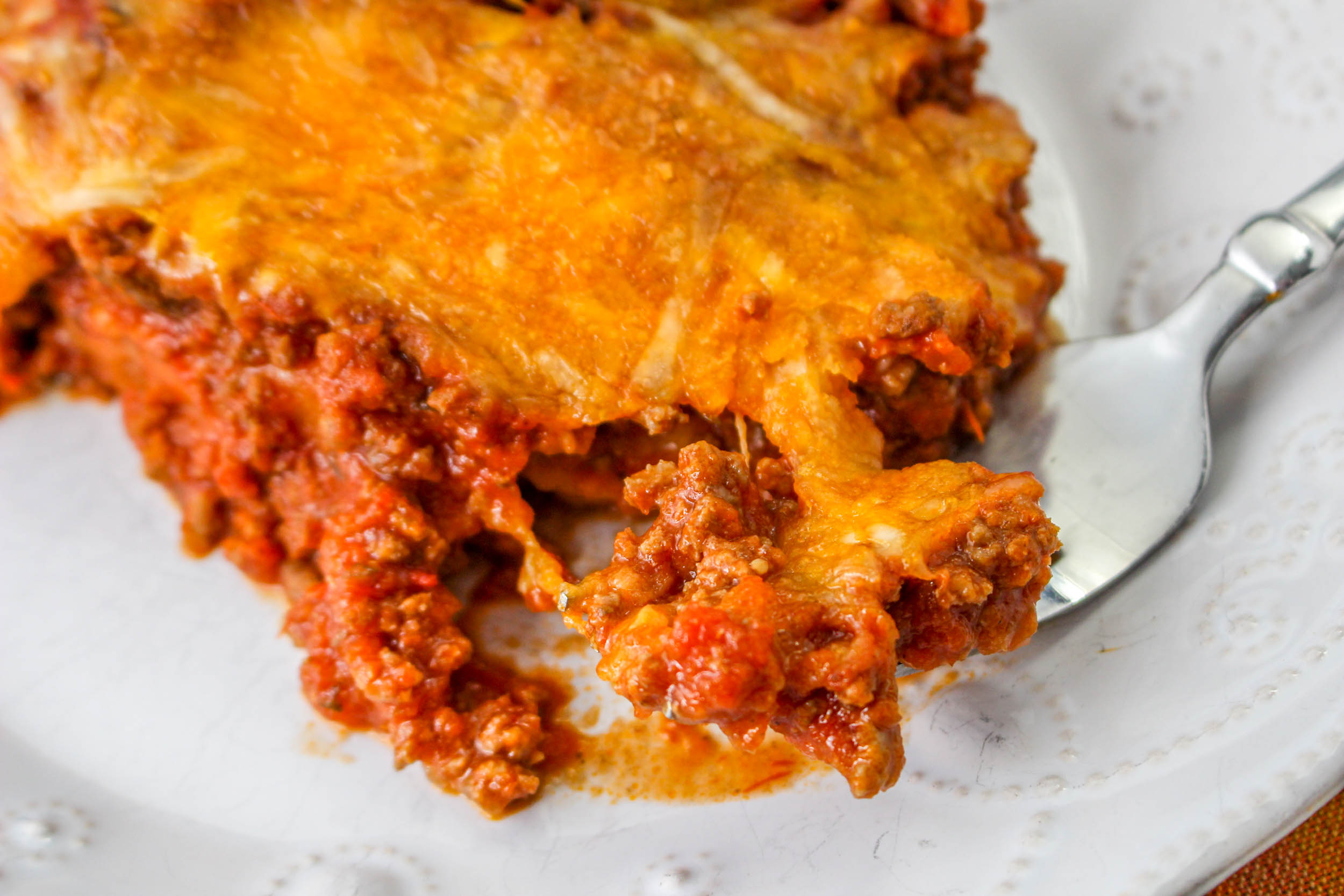 A close-up of a serving of cheesy ground beef casserole on a white plate with a fork.