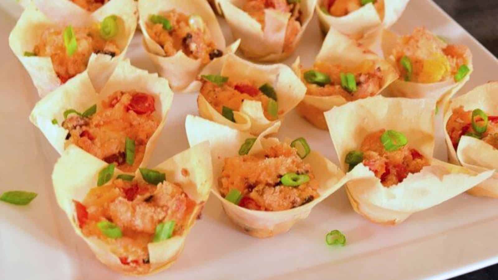 Wonton cups filled with a creamy mixture, topped with chopped green onions, arranged on a white plate.