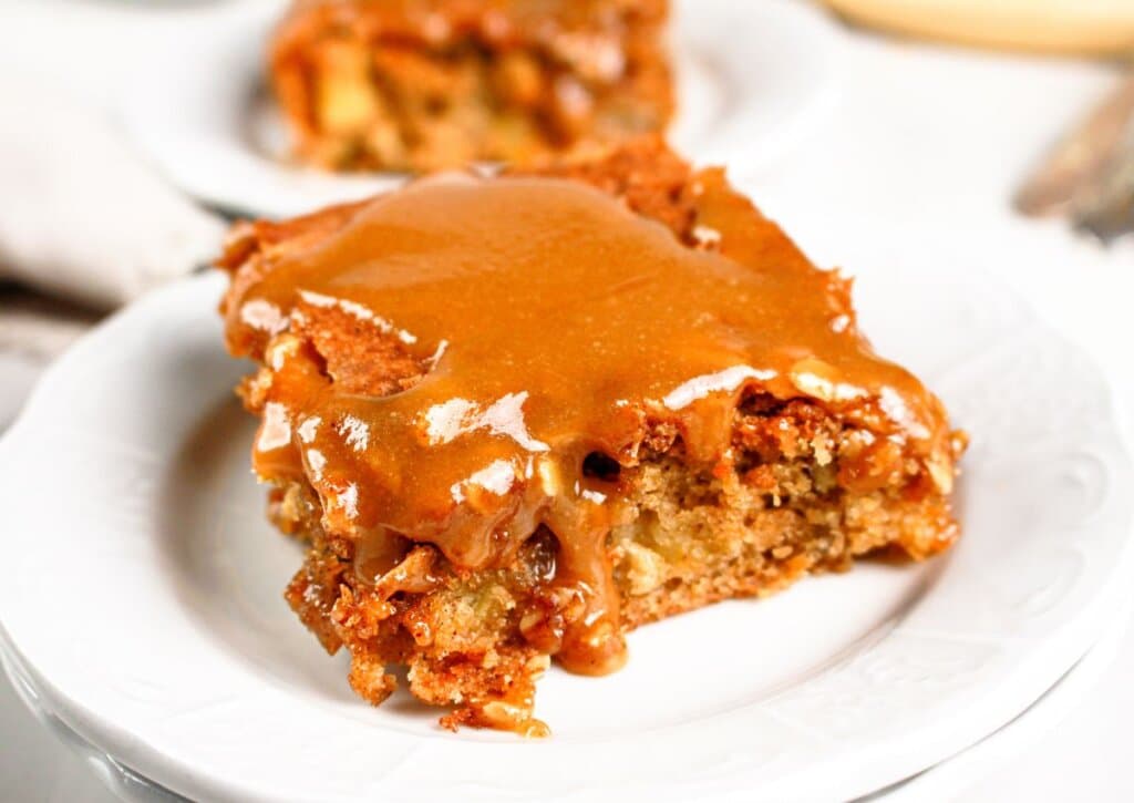 A square piece of cake with a caramel glaze is served on a white plate.