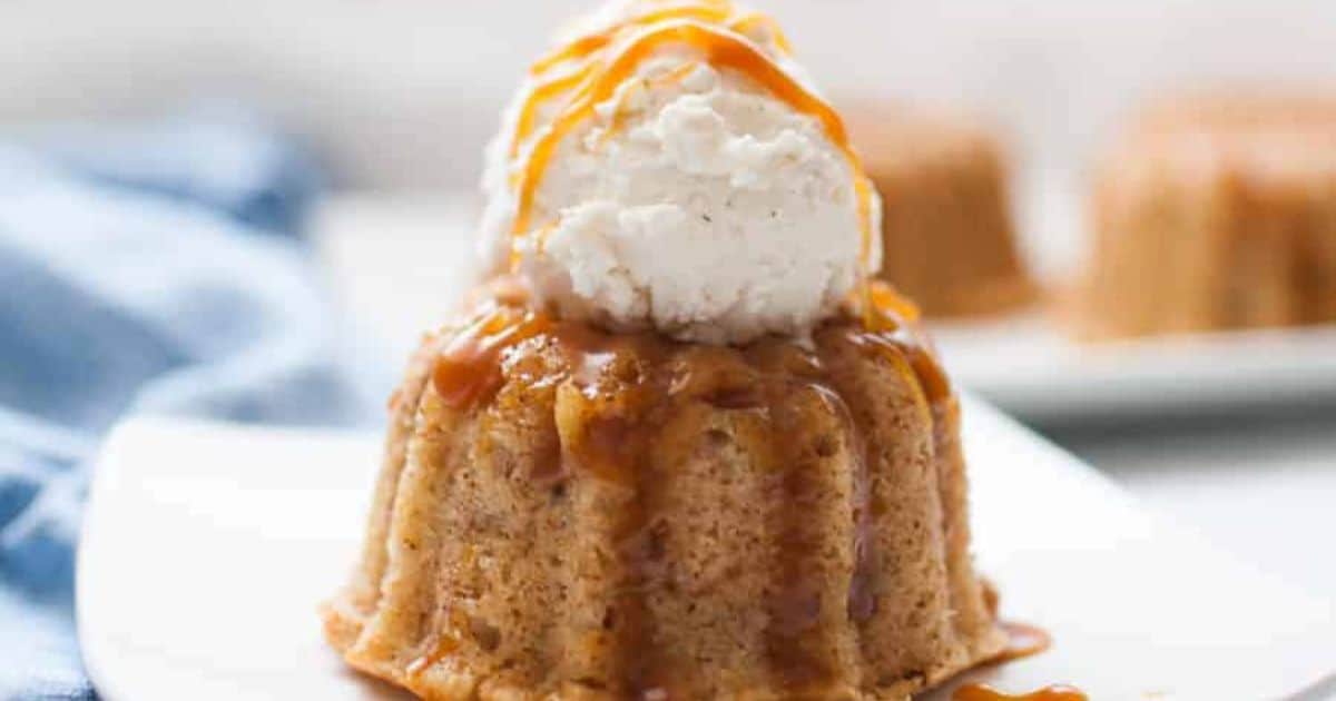 A small bundt cake topped with a scoop of vanilla ice cream and drizzled with caramel sauce, served on a white plate.