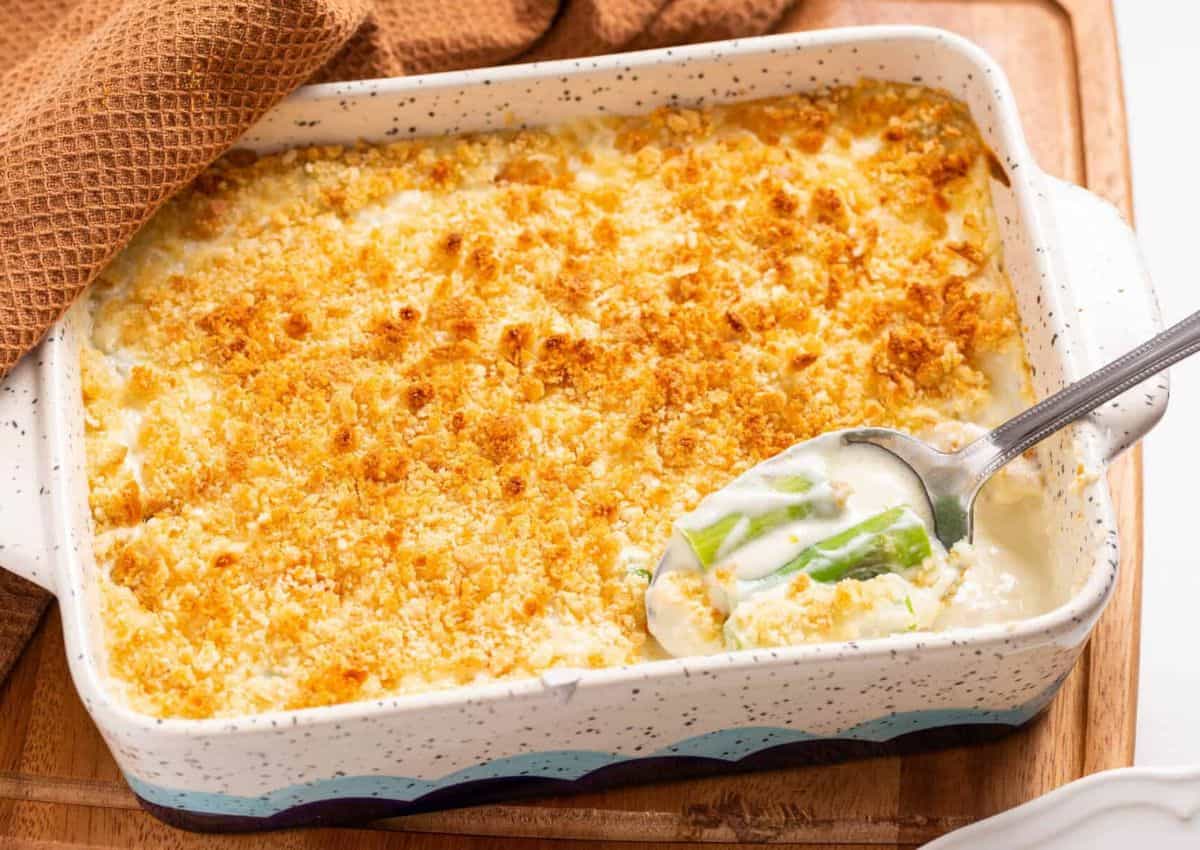 A casserole dish filled with creamy, baked casserole topped with a golden breadcrumb crust, with a serving spoon showing the filling inside.