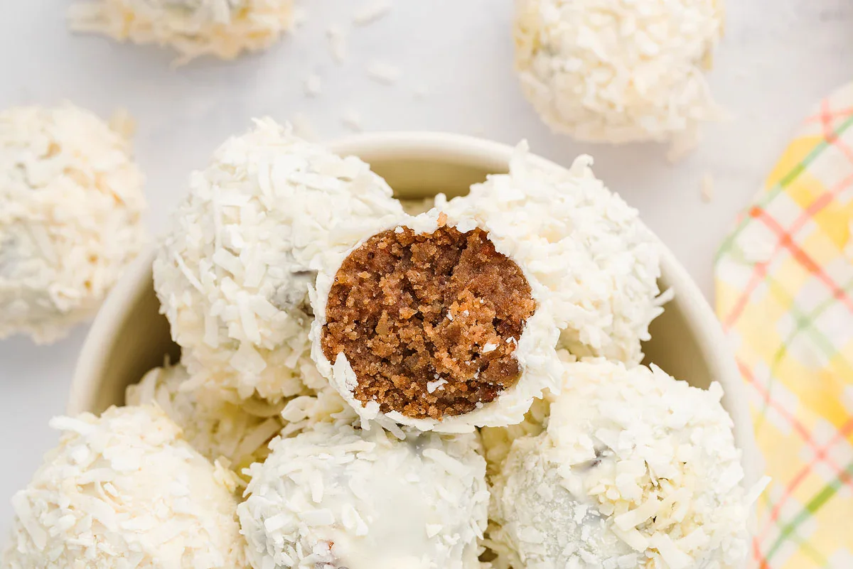 A bowl of white coconut-covered dessert balls, with one ball cut open to show its brown, crumbly interior.