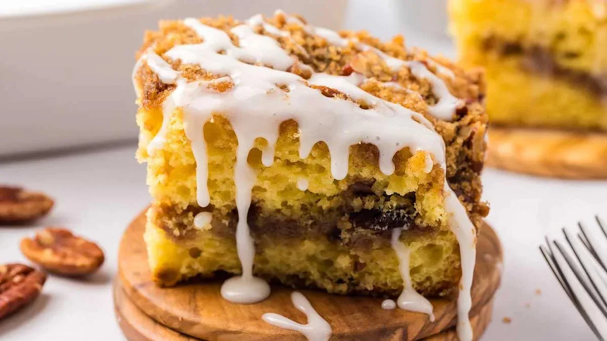 A close-up of a slice of coffee cake with a crumb topping and white icing drizzled on top, placed on a small wooden board.