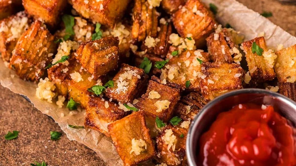 Crispy golden potato cubes topped with grated cheese and herbs, served on parchment paper with a side of ketchup.