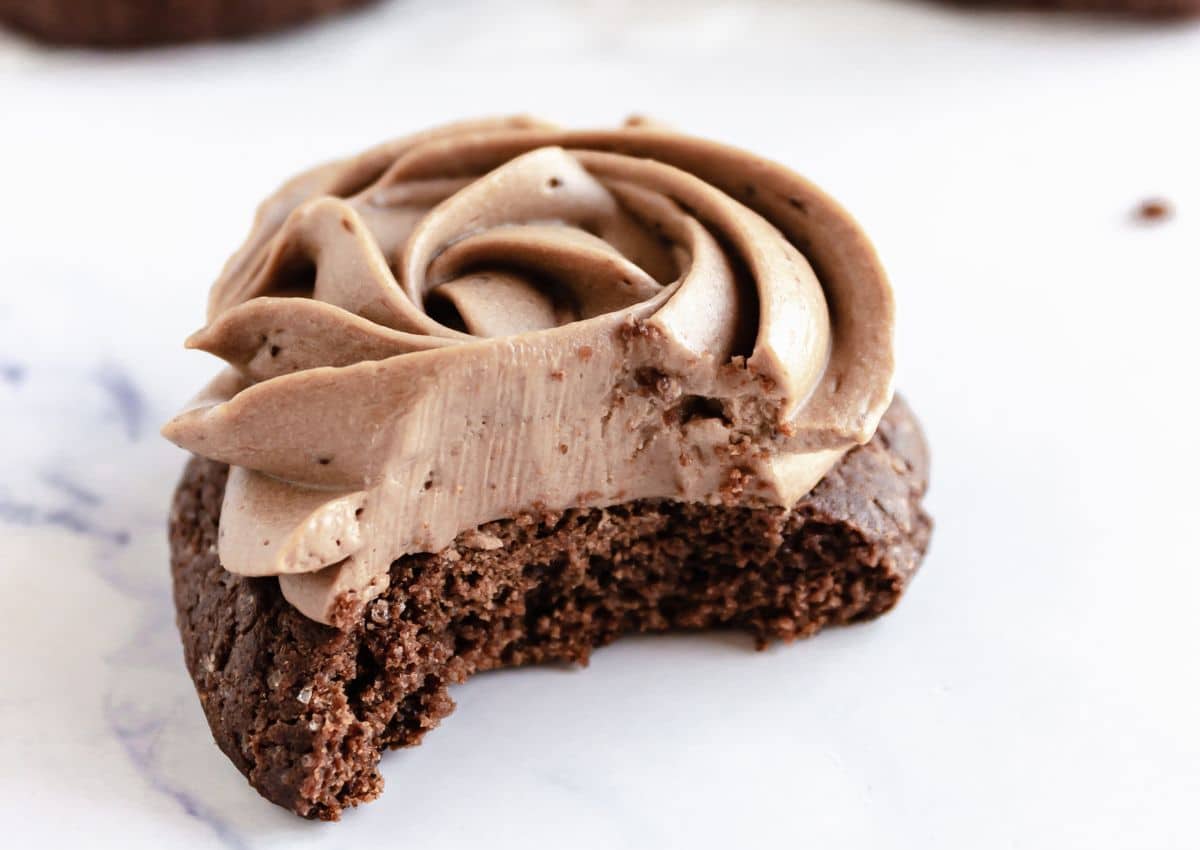 A chocolate cookie with a swirl of chocolate frosting on top, shown with a bite taken out of it.