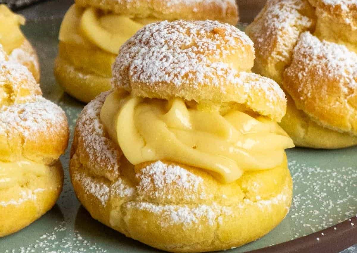 Cream puffs filled with custard cream are topped with powdered sugar and arranged on a plate.