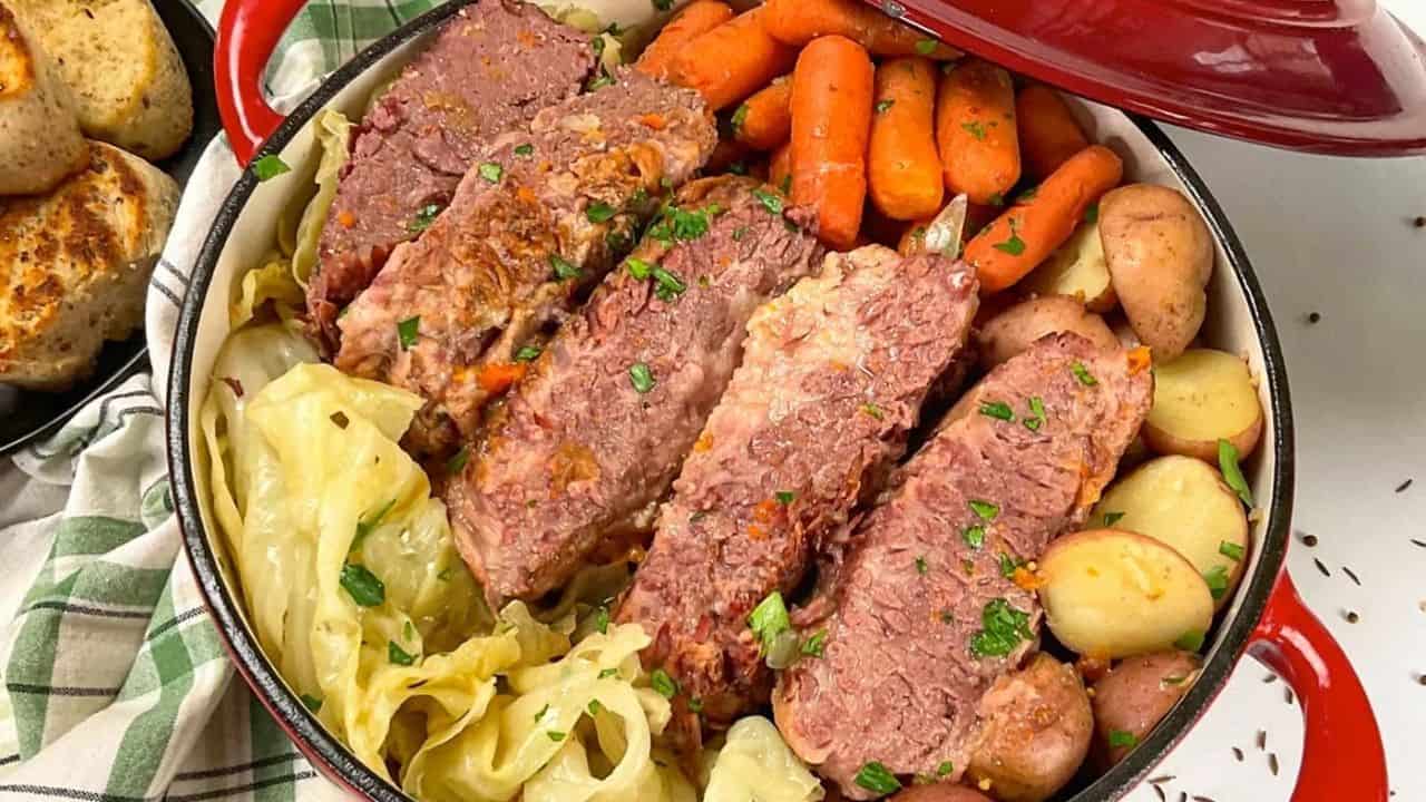 A pot filled with sliced corned beef, baby carrots, red potatoes, and cabbage, garnished with chopped parsley.
