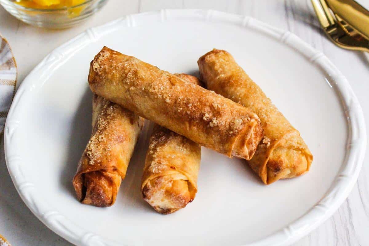 Four golden-brown, crispy lumpia rolls are arranged on a white plate.