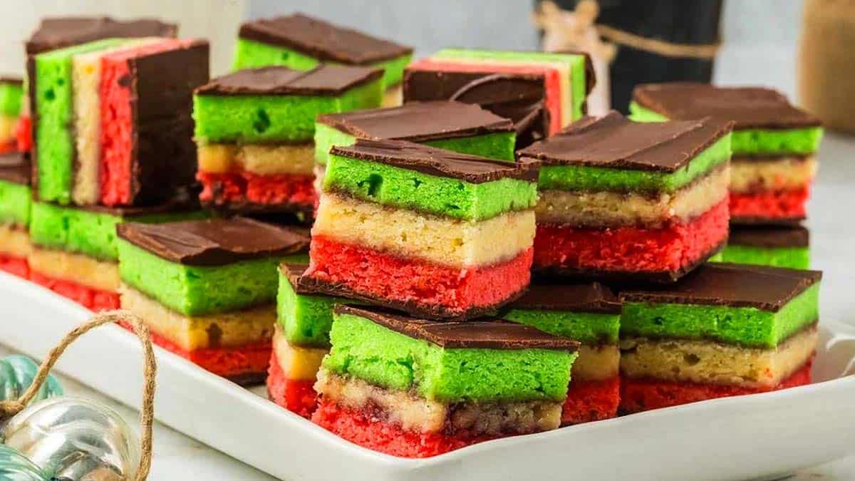 A plate of layered Italian rainbow cookies with green, yellow, and red layers, topped with a layer of chocolate.