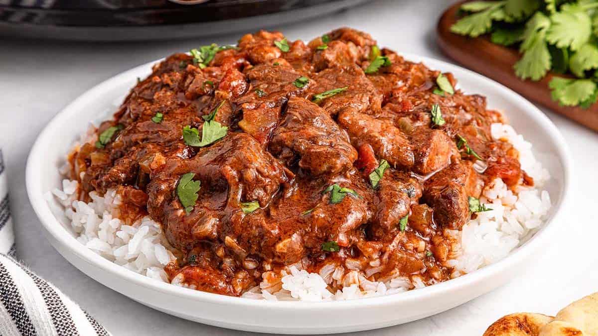 A plate of white rice topped with beef stew in a rich, brown sauce, garnished with fresh cilantro.