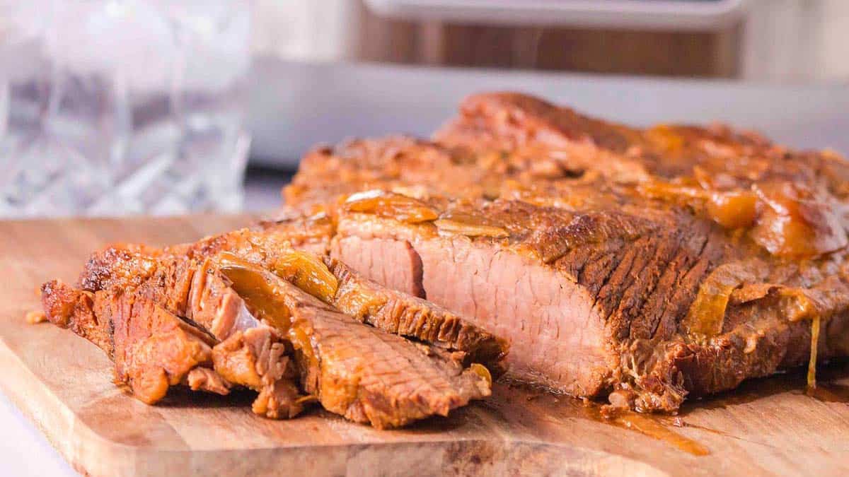 Sliced cooked brisket on a wooden cutting board, showing juicy, tender meat with a browned exterior.