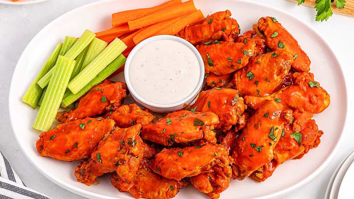 A platter of buffalo chicken wings garnished with herbs, served with celery, carrot sticks, and a cup of ranch dressing.