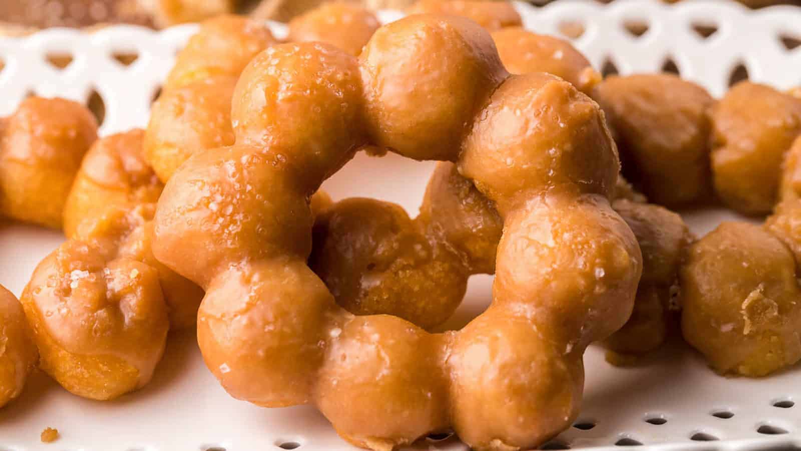 A close-up of glazed mochi donuts with a ring shape, arranged on a white perforated tray.