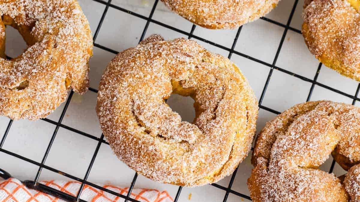 Sugary baked donuts are arranged on a black cooling rack, viewed from above.