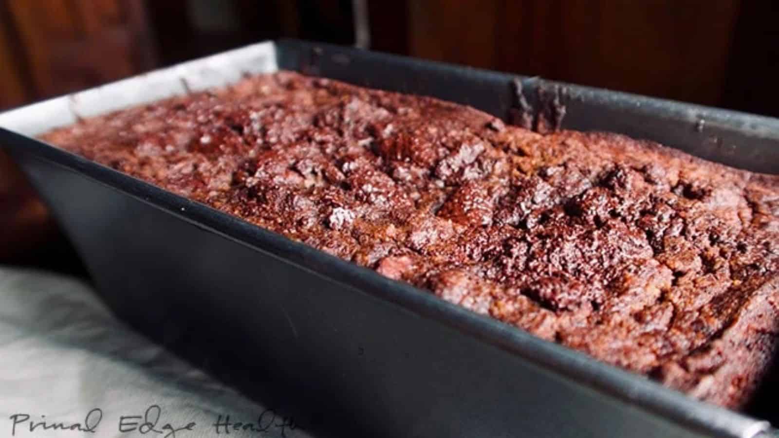 A freshly baked chocolate loaf cake in a black rectangular pan, with a textured, slightly cracked top.