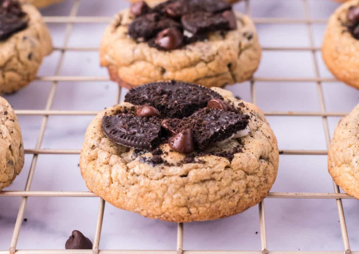 A chocolate chip cookie topped with crumbled chocolate sandwich cookies and chocolate chips on a cooling rack.
