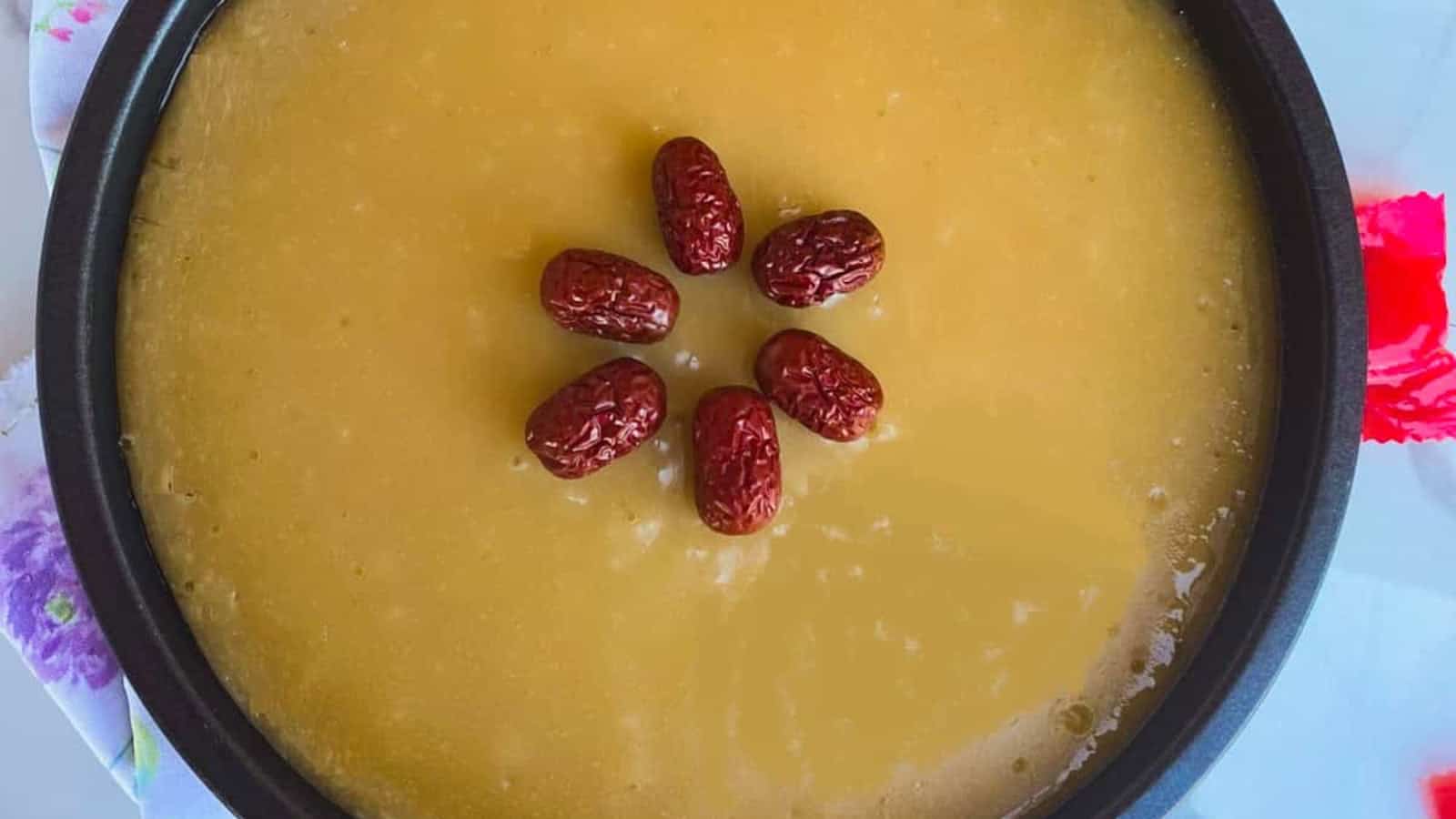 A bowl of yellow pudding topped with six red dates arranged in a circular pattern in the center.