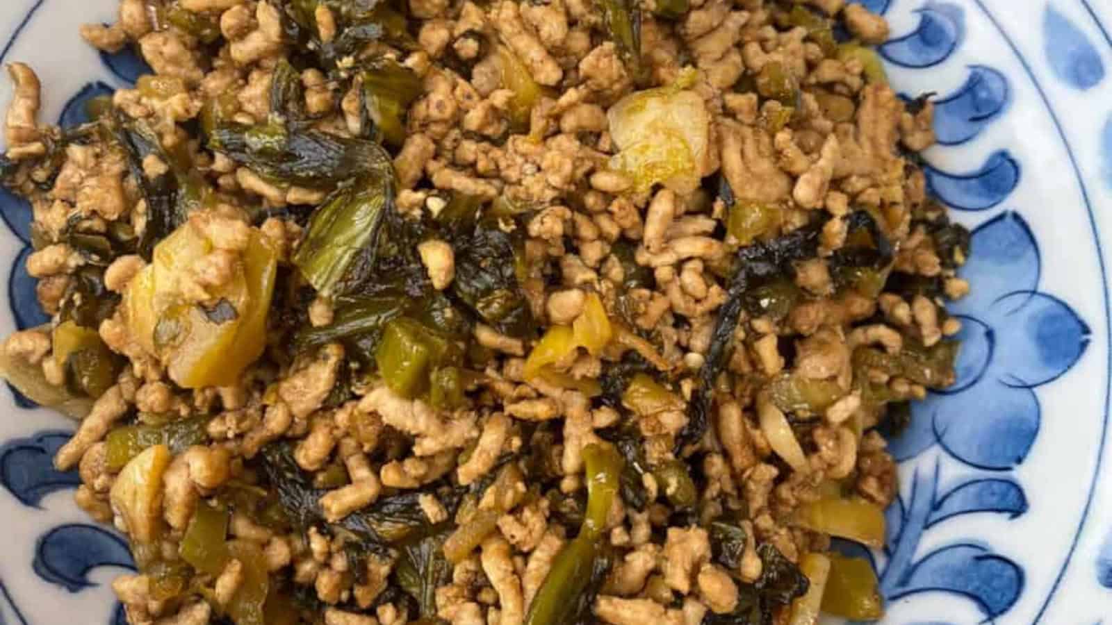 A plate of minced pork stir-fried with chopped preserved mustard greens on a blue and white dish.