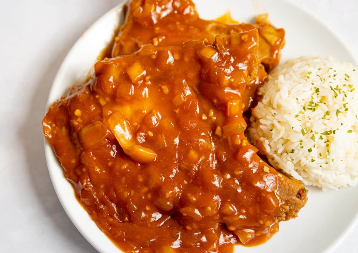 A plate with thin pork cutlets covered in brown onion gravy, served with a mound of white rice garnished with herbs.