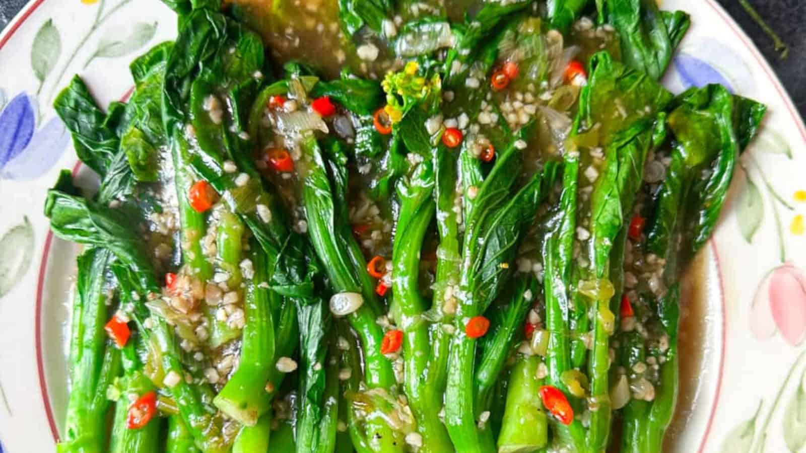 A plate of cooked leafy green vegetables topped with minced garlic, chopped red chili, and a savory sauce.